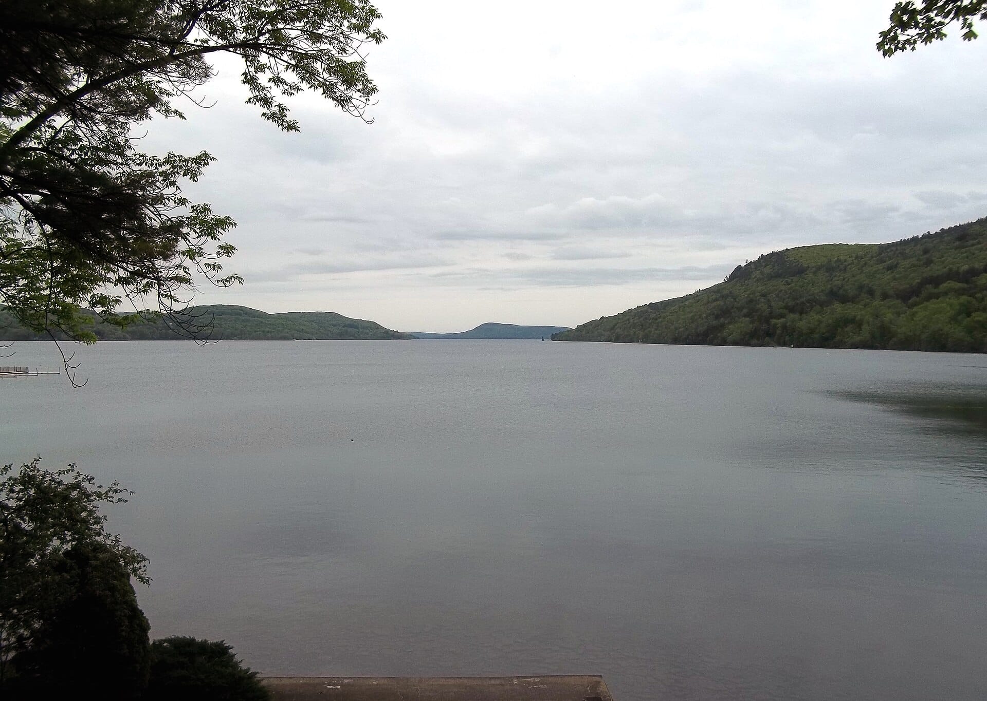 Otsego Lake stretching north from Cooperstown, New York, between wooded hills under a soft grey sky