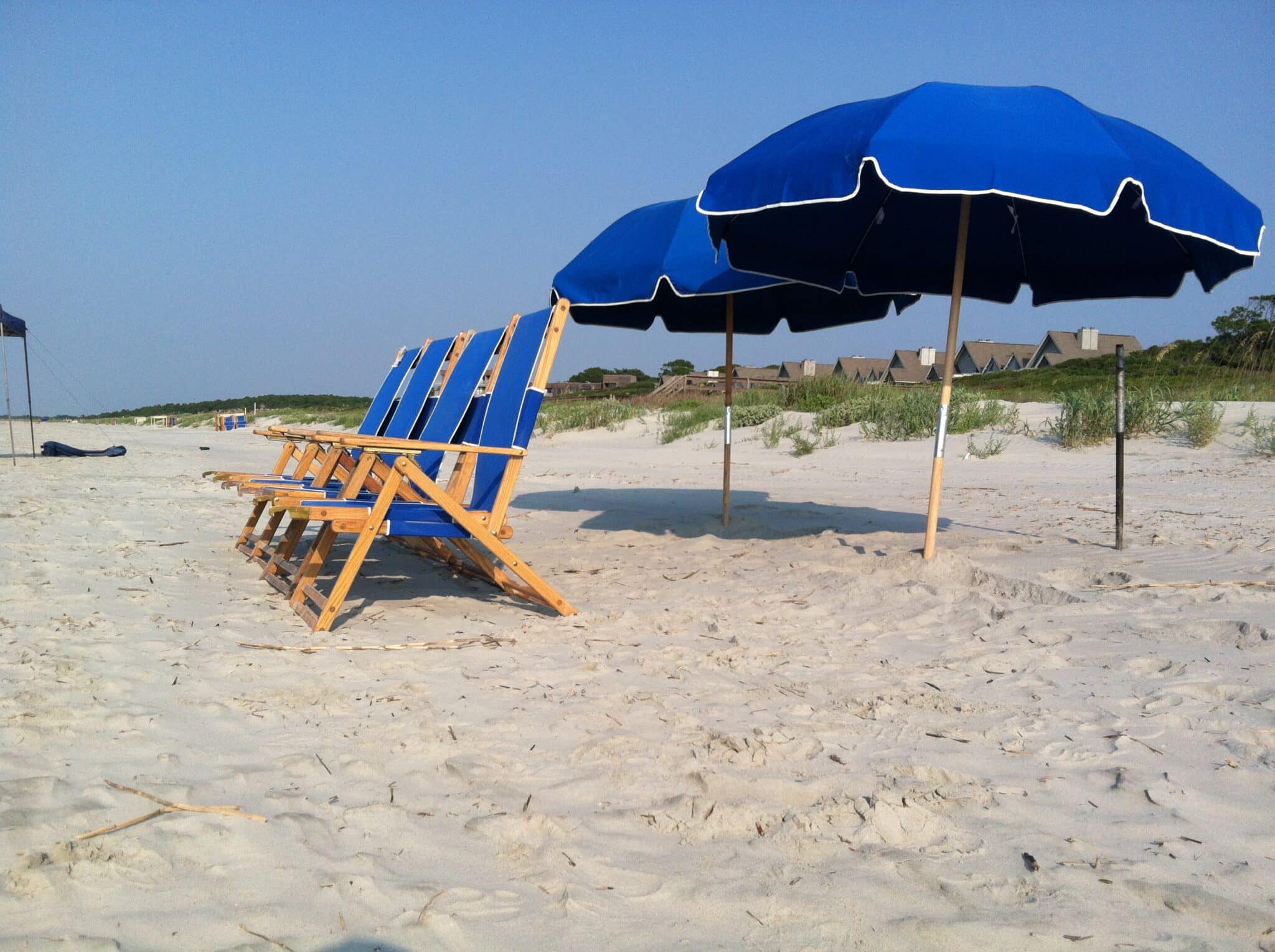 Blue beach umbrellas and wooden beach chairs set up on soft sand on the South Carolina coast